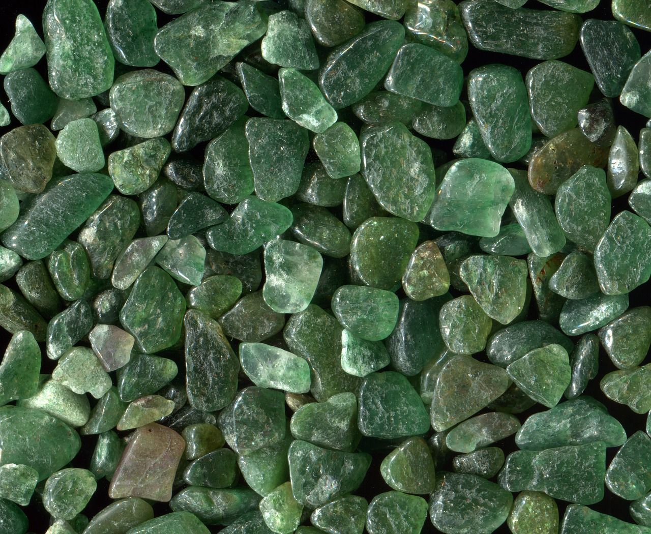 A pile of green rocks on a black surface. Green quartz