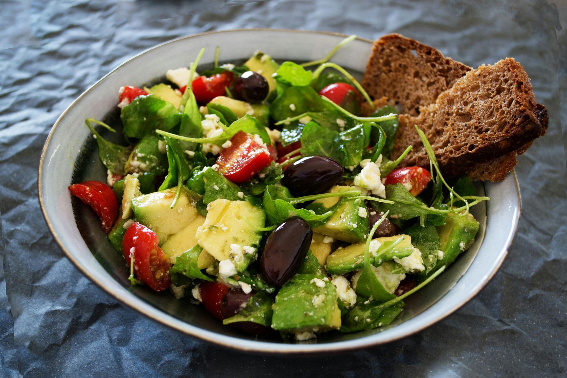 A bowl of salad with a piece of bread on the side