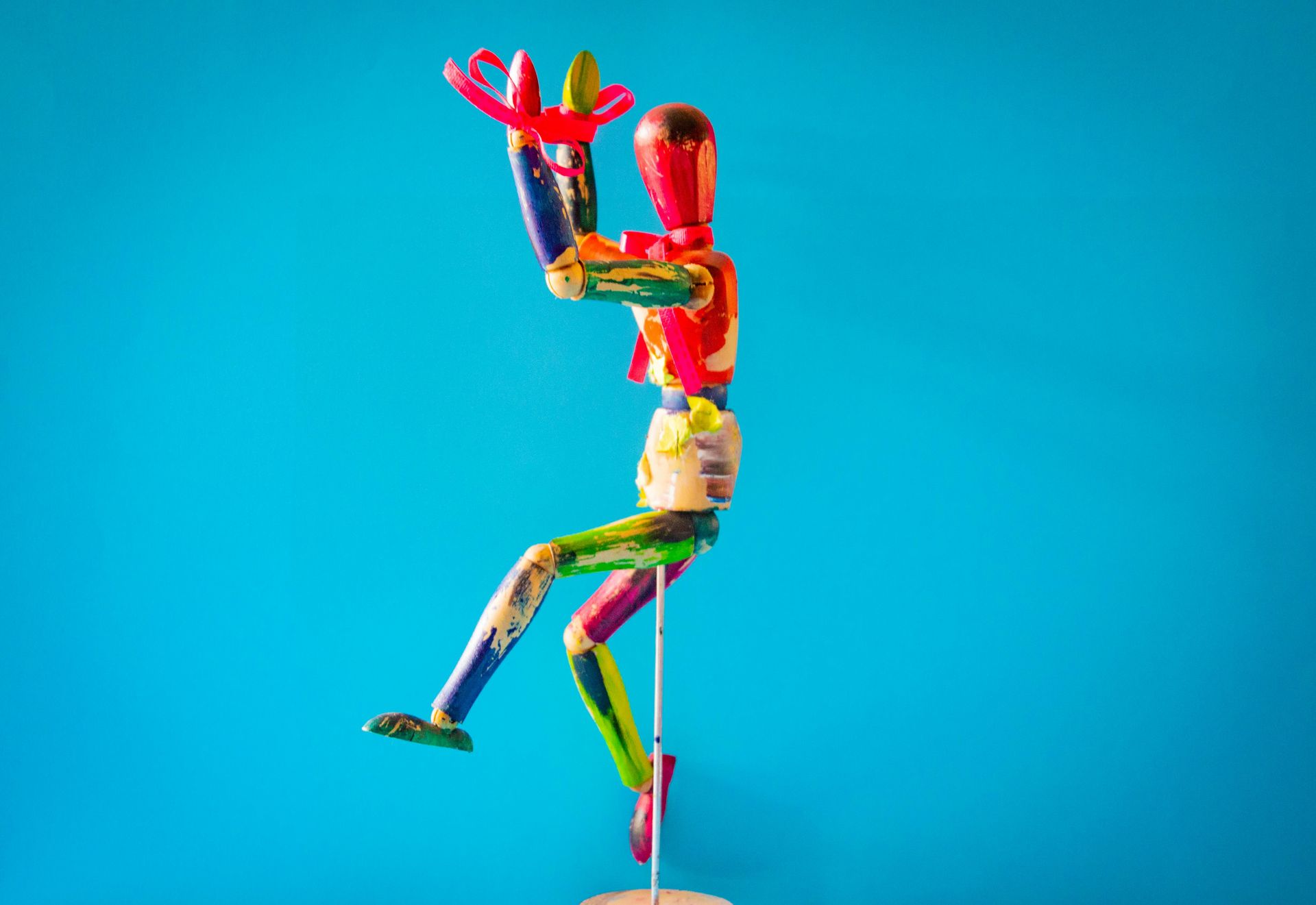 Colorful wooden artist's mannequin posed with arms raised, on a blue background.