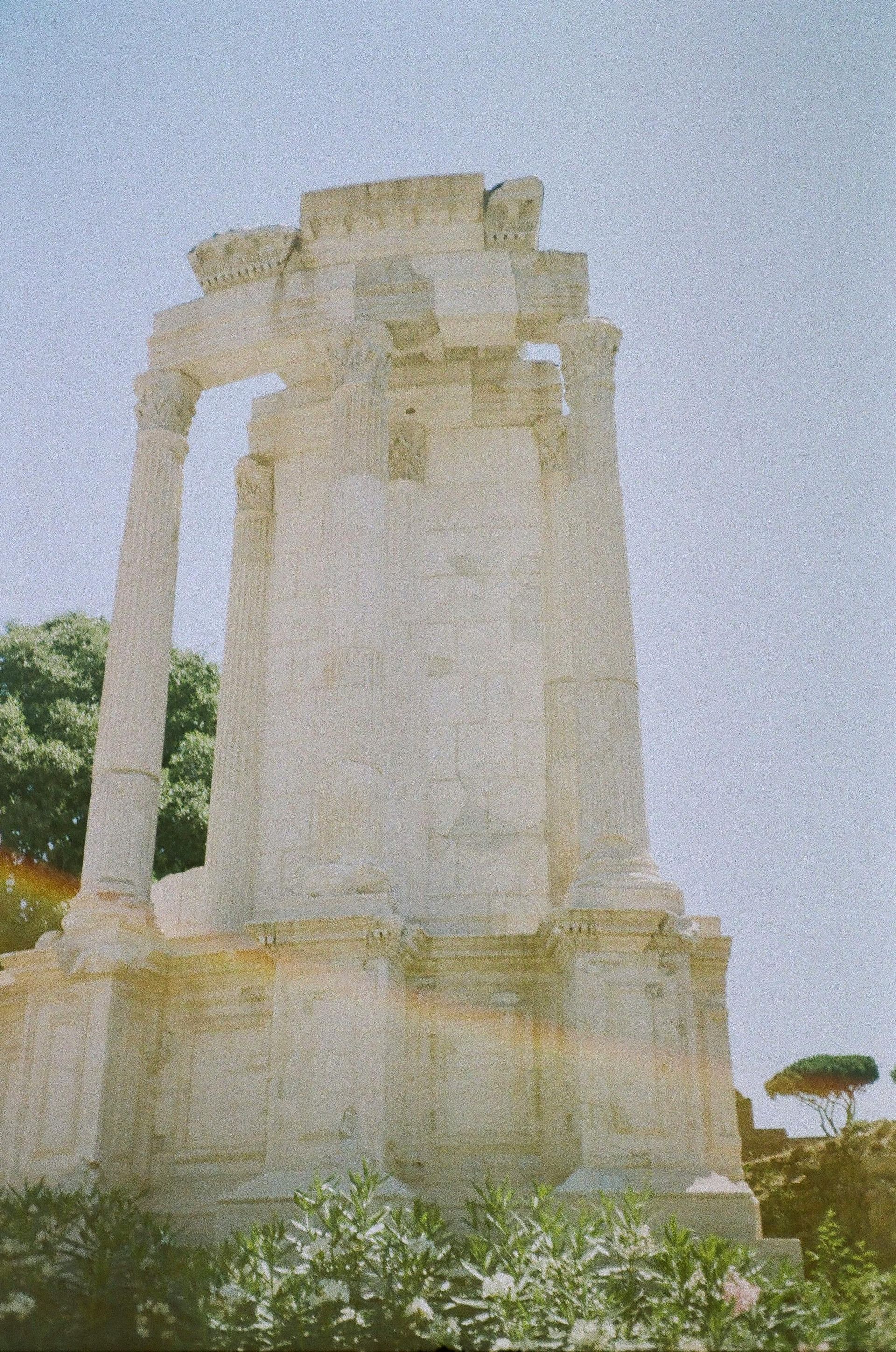 Ancient Roman ruin of a white stone temple and arch with a blue sky in the background.