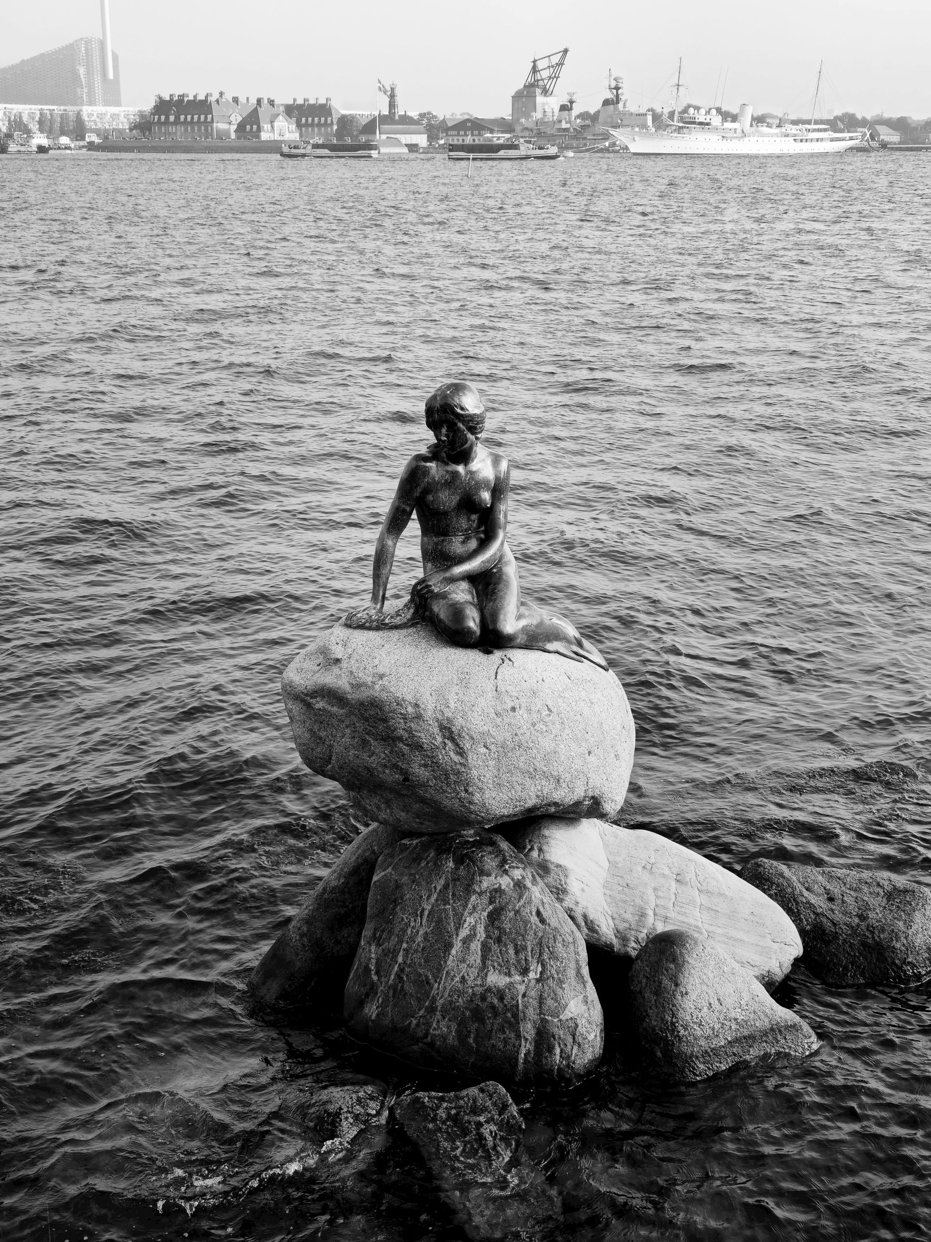 A statue of a mermaid is sitting on top of a rock in the water.