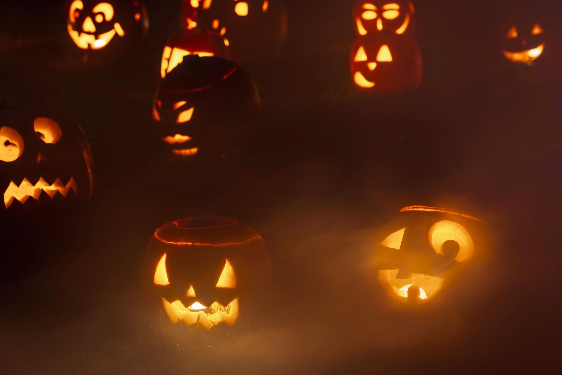 Glowing jack-o'-lanterns with carved faces in the fog, lit from within.
