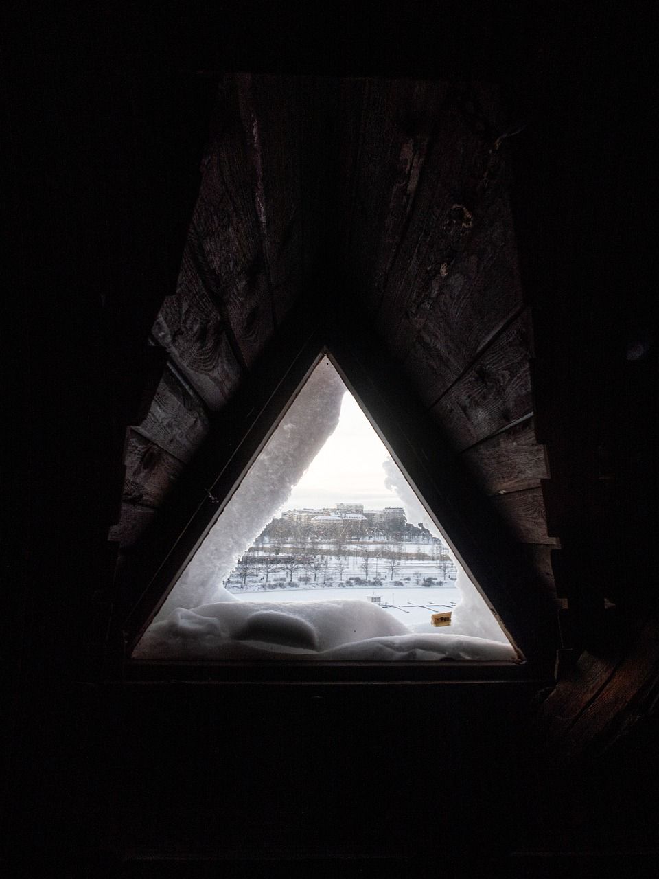 A view of a snowy landscape through a triangle window.