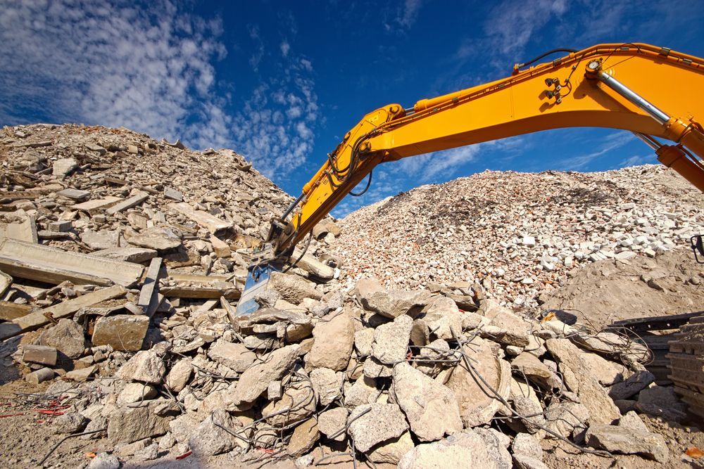 A Yellow Excavator Is Working On A Pile Of Rocks — Dubbo Hardcore Soils & Earthmoving In Dubbo, NSW