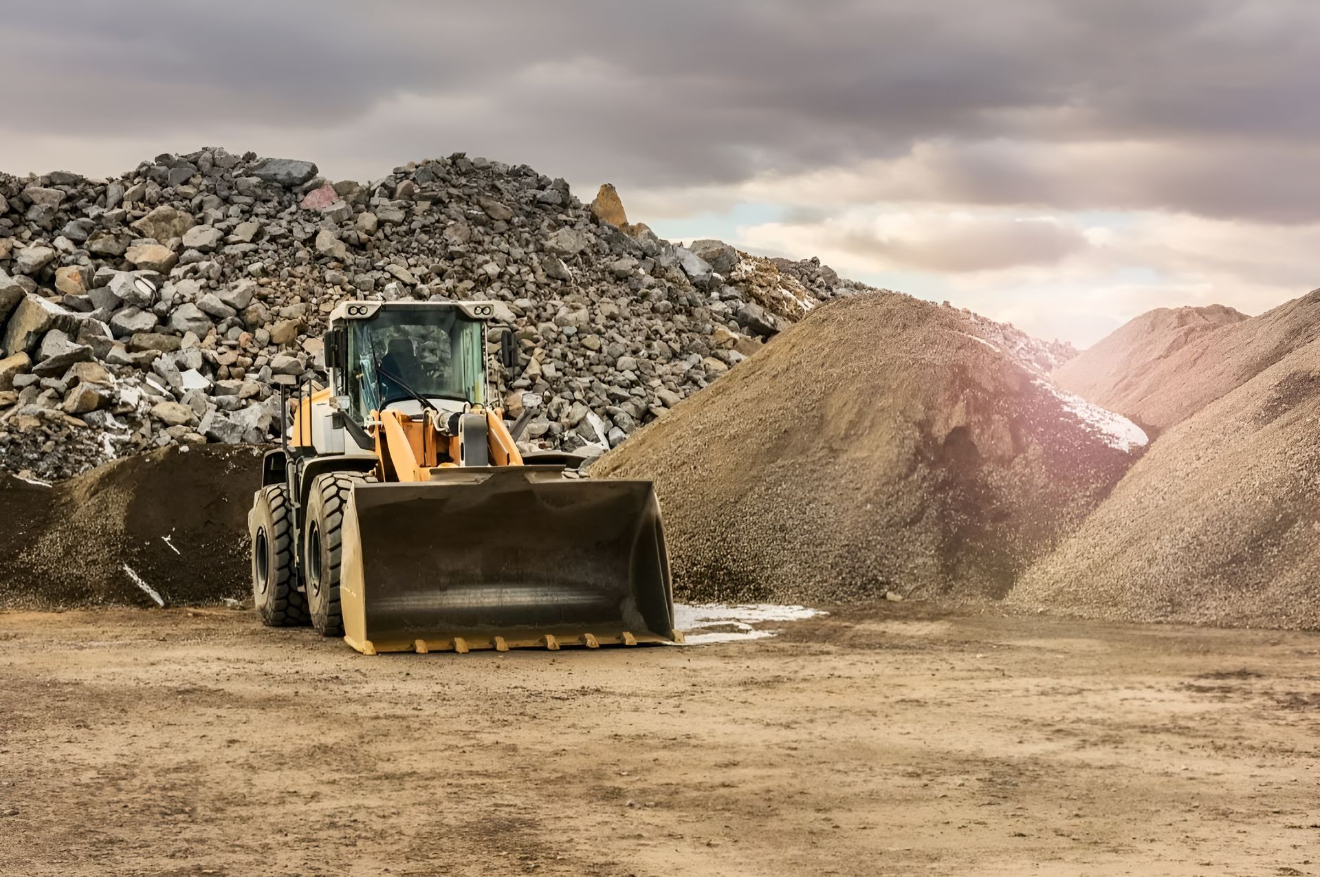 A Bulldozer Is Driving Through A Dirt Field In Front Of A Pile Of Rocks — Dubbo Hardcore Soils & Earthmoving In Dubbo, NSW