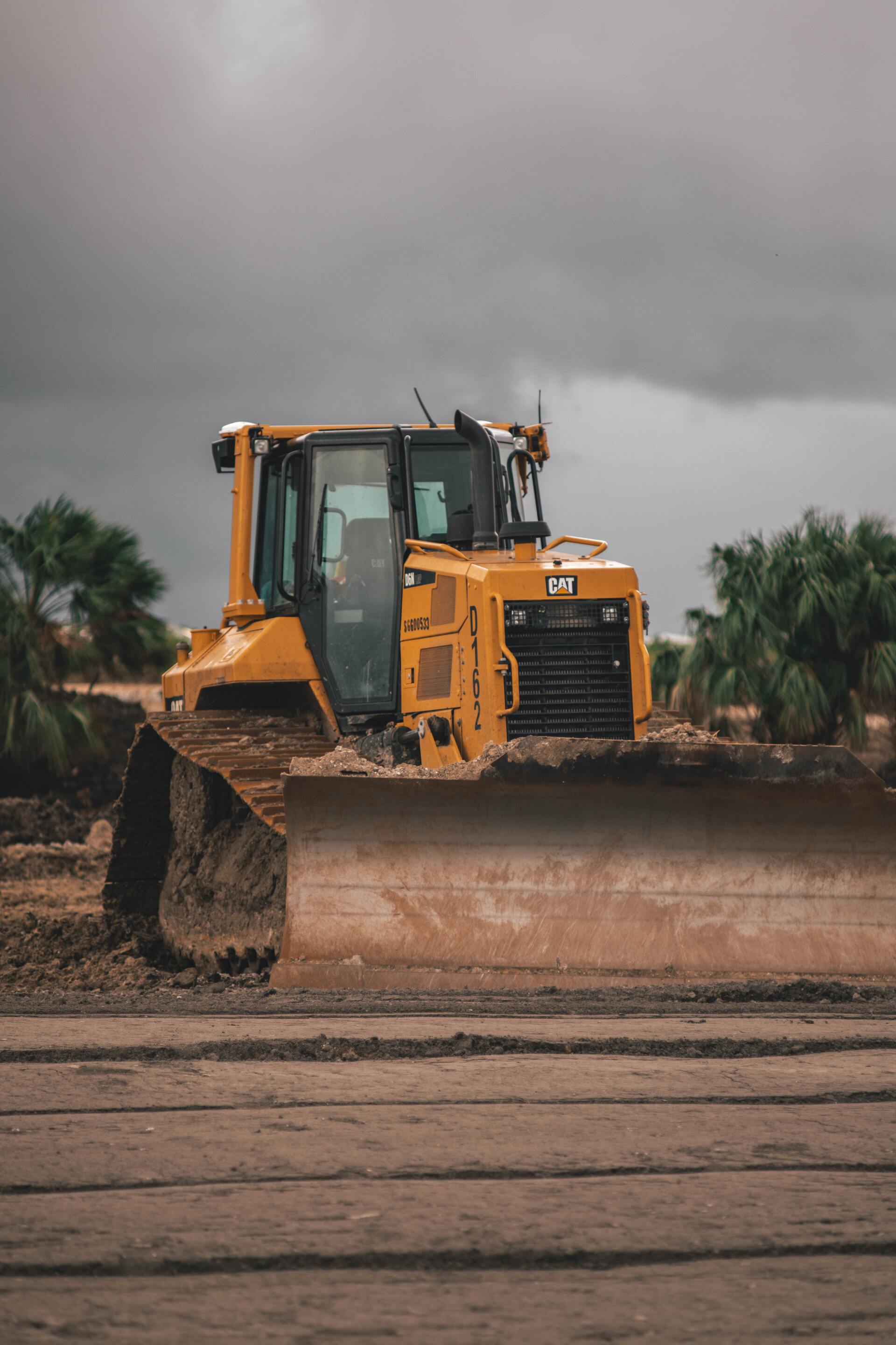 A Bulldozer Is Driving Through A Dirt Field On A Cloudy Day — Dubbo Hardcore Soils & Earthmoving In Dubbo, NSW