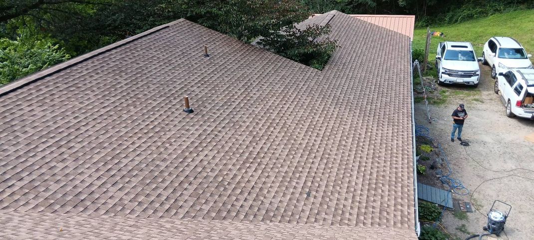 Large shingled roof beside a gravel driveway with parked cars and a person standing nearby.