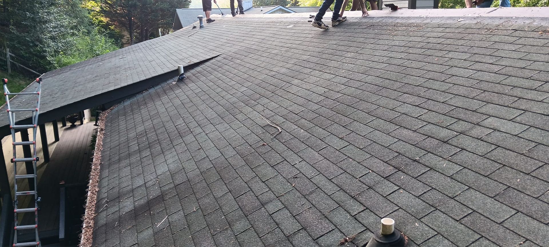 Workers on a sloped shingled roof inspecting or repairing the surface near the edge