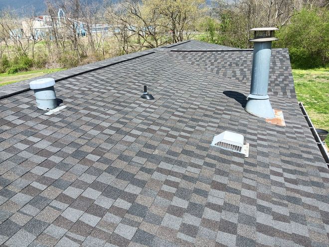 Rooftop with gray shingle tiles, vents, and a chimney, with trees and greenery in the background