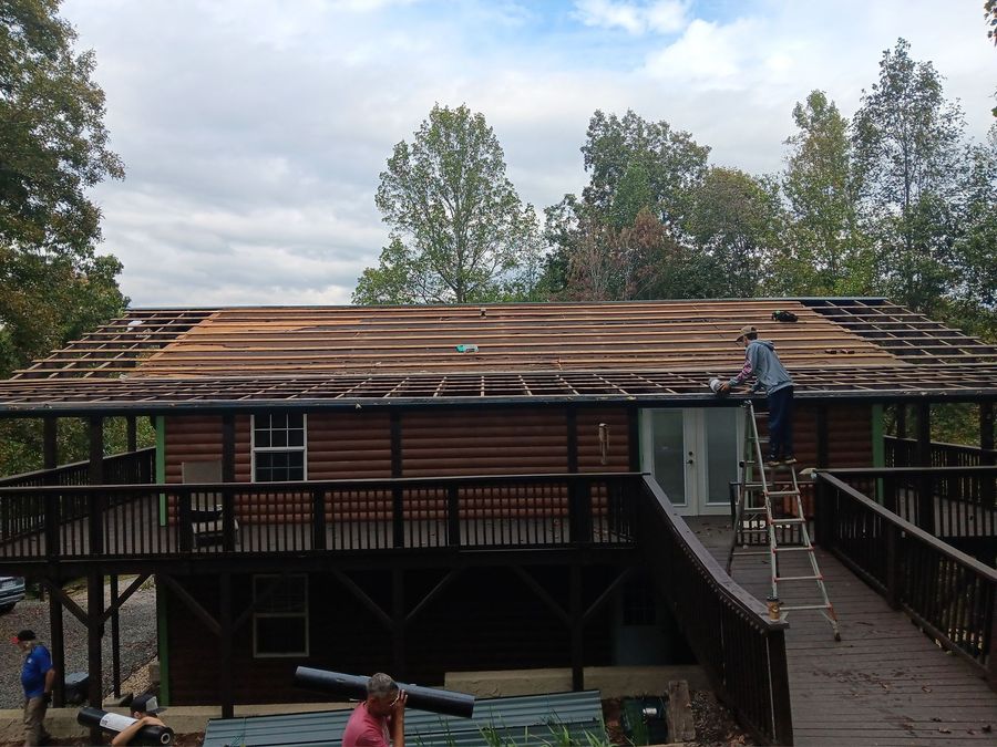 Workers repairing a sloped roof on a two-story building with stairs and railings