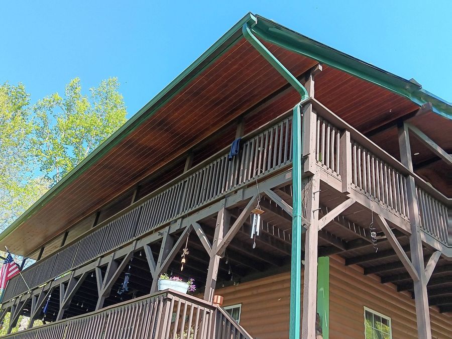 Wooden lodge with wraparound balcony and green roof against a blue sky, viewed from below