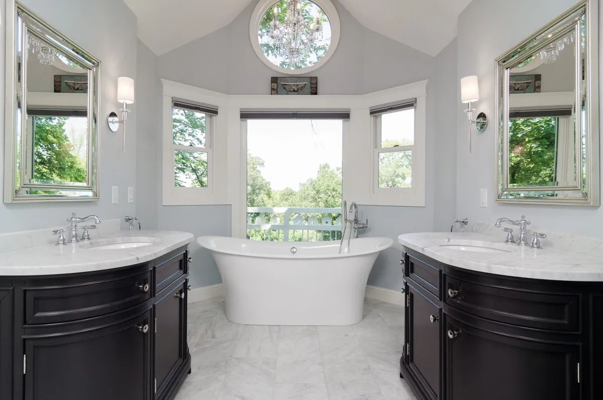 A bathroom with two sinks , a tub and a window.
