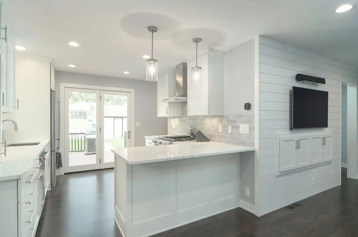 A kitchen with white cabinets and a flat screen tv on the wall.