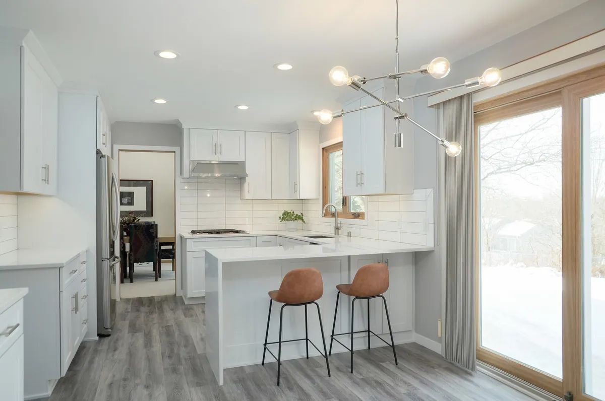 A kitchen with white cabinets , stools , a sliding glass door and a chandelier.