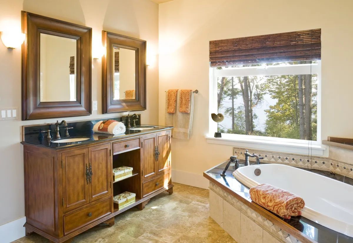 A bathroom with a tub , sinks , mirrors and a window.
