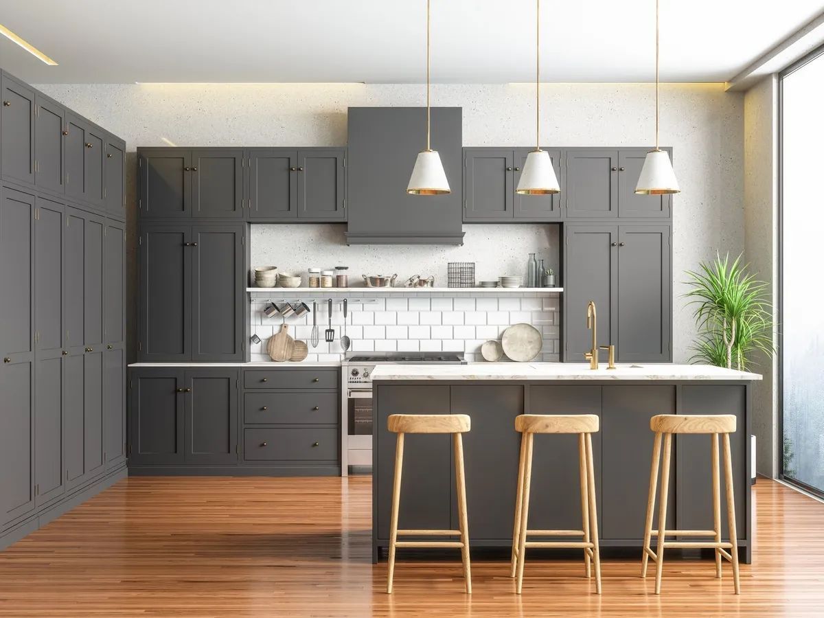 A modern kitchen with gray cabinets , wooden floors , stools and a large island.