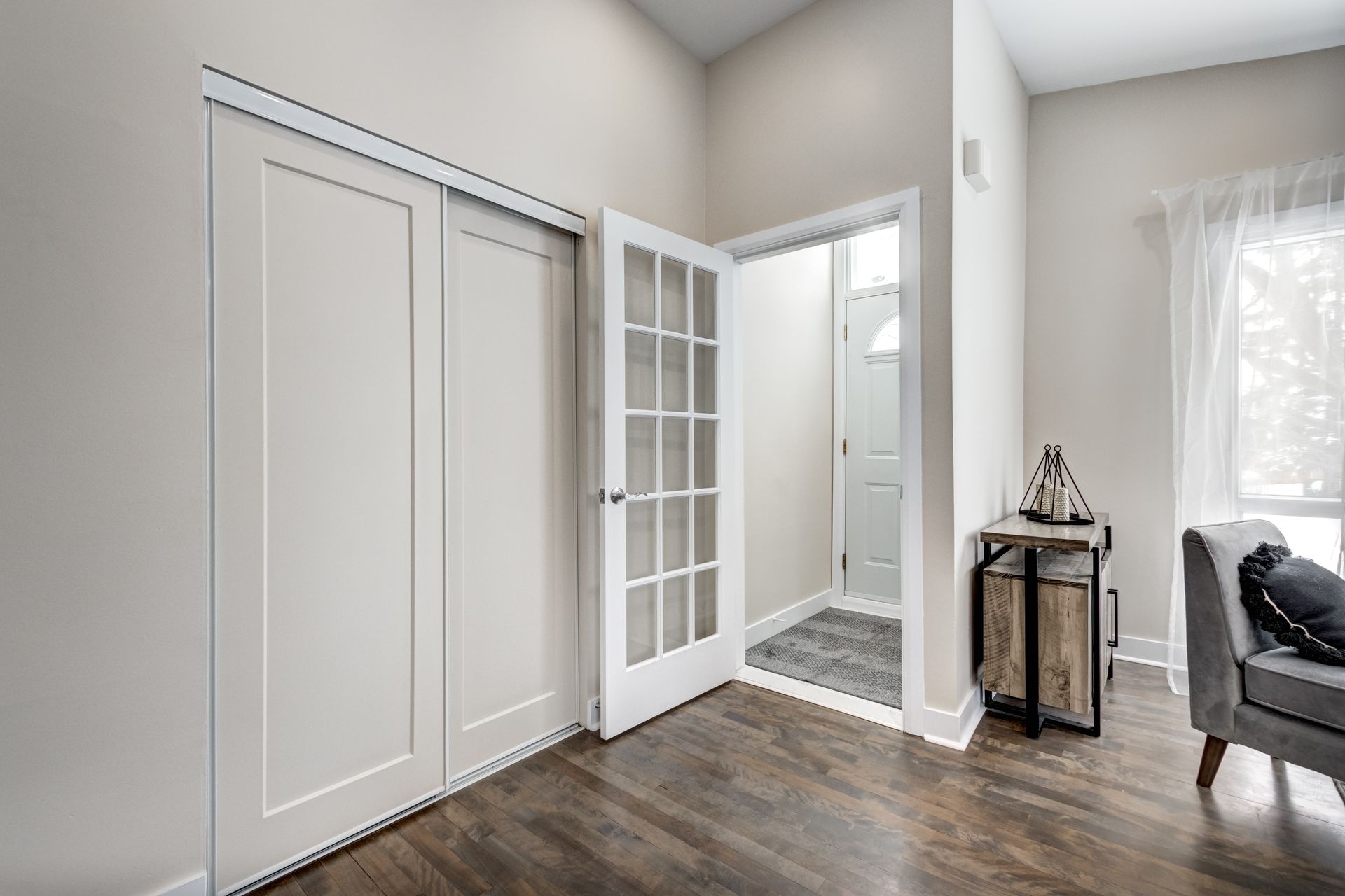 A living room with hardwood floors , white walls and a french door leading to a bathroom.