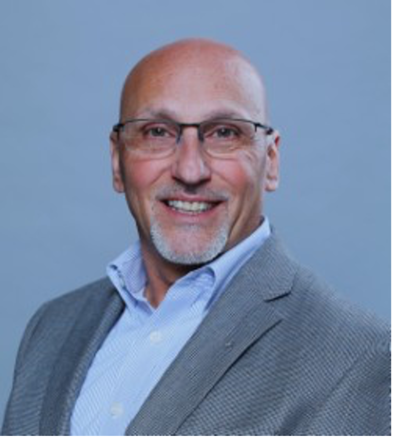 Dr. Ben Litalien with glasses, smiling, wearing a grey suit jacket and blue shirt against a grey backdrop.