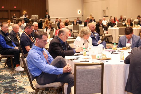 A conference room filled with people seated at tables and praying.