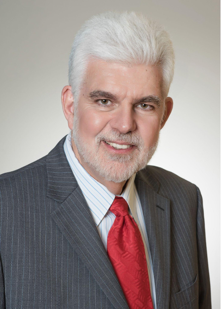 Dr. John Hayes with gray hair and beard in a suit and red tie smiles.