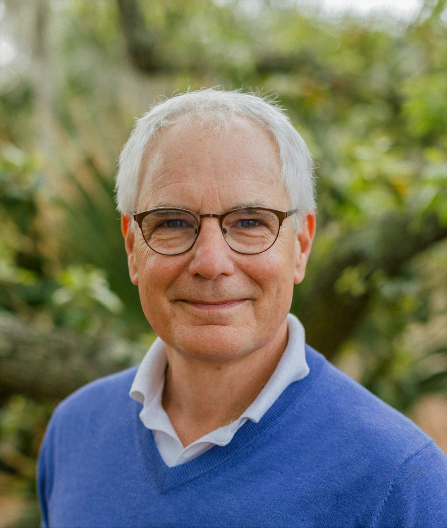 Lloyd Reeb with glasses and gray hair smiles in a blue sweater, outdoors.