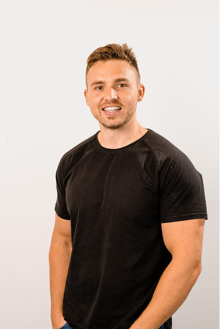 Matt Hayes in a black shirt smiling, arms at sides. White background.