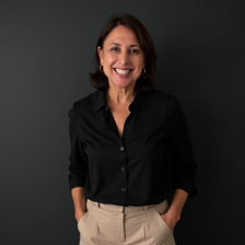 Nicole Neesen with dark hair, smiling, wearing a black shirt and tan pants, hands in pockets.