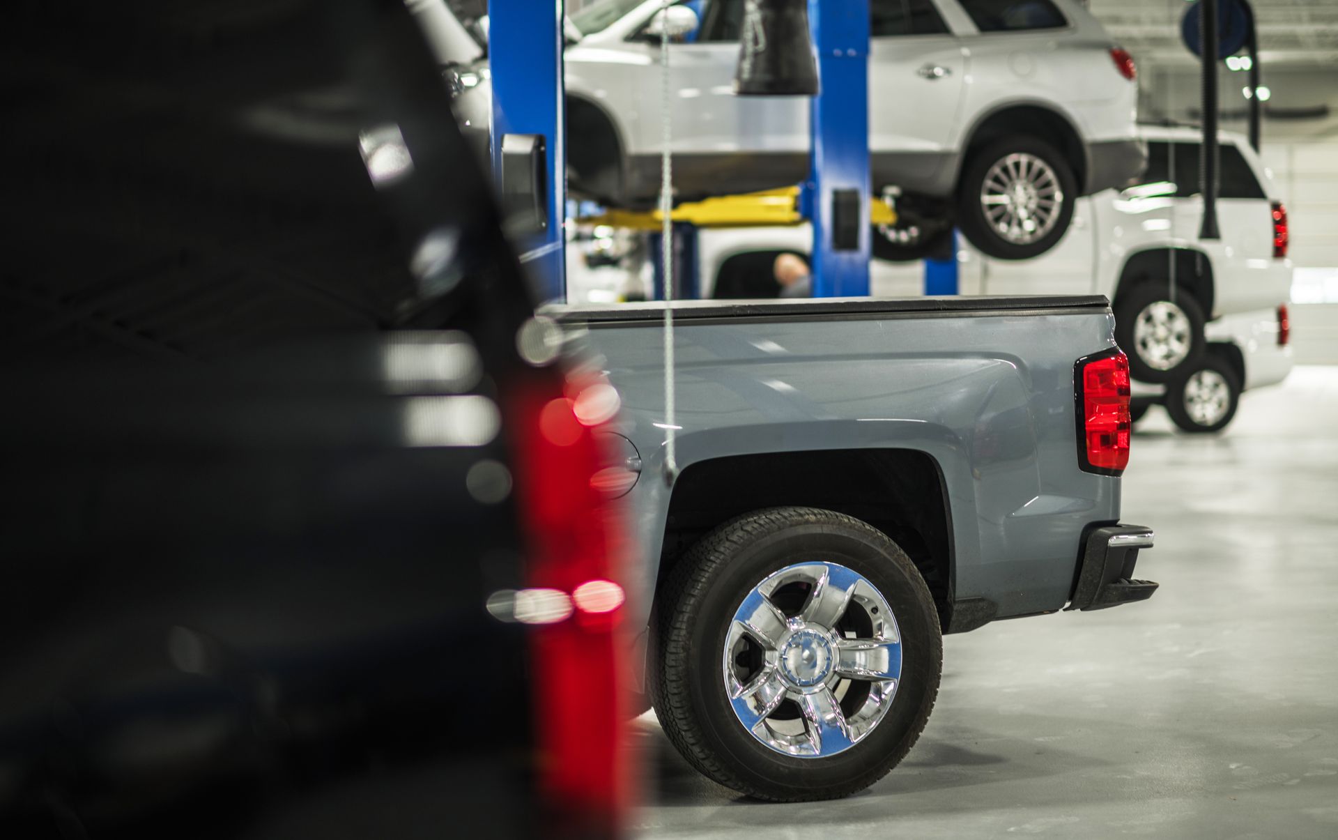 Pickup trucks parked in a bright auto service garage, with a dark truck in the foreground