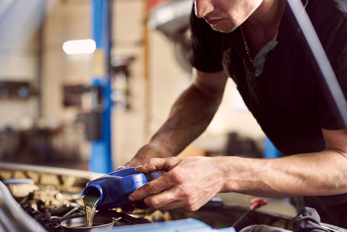 Mechanic pouring oil into a car engine in a garage.
