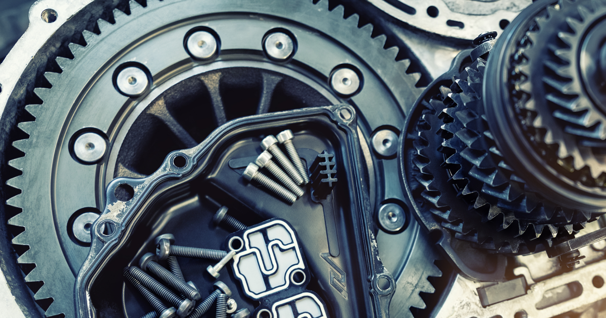 Close-up of disassembled automotive transmission components, including gears, bolts, and a cover.