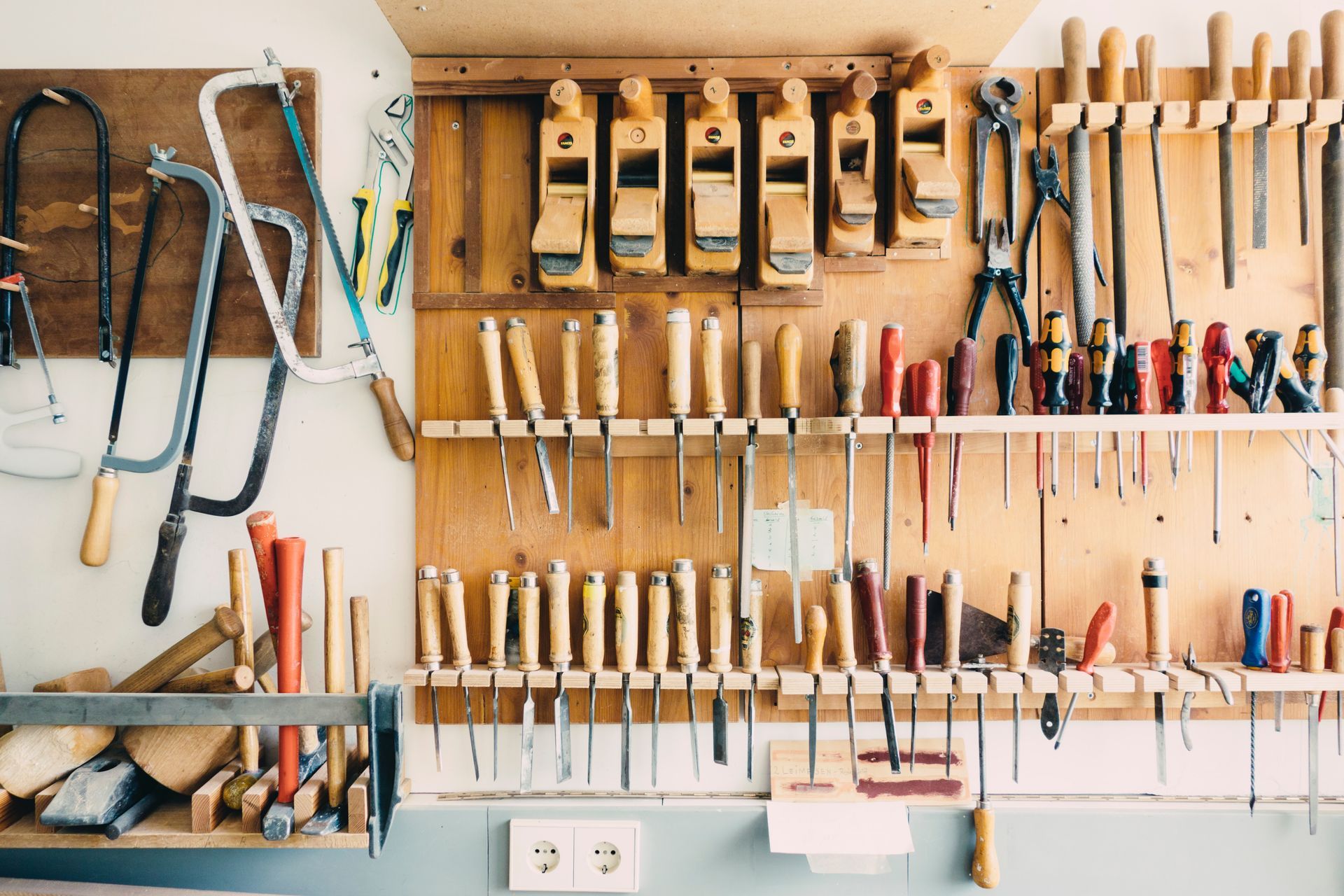 Assorted handheld tools neatly organized on a tool rack, including screwdrivers, pliers, saws, and hammers.
