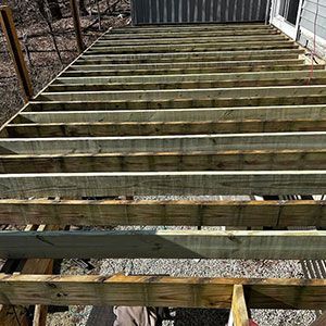 A high-angle view of a wooden deck frame under construction with parallel joists extending from a house wall.