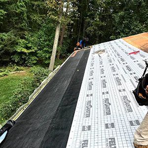 A view from a sloped roof showing installed black roofing underlayment and white grid-pattern GAF FeltBuster rolls.