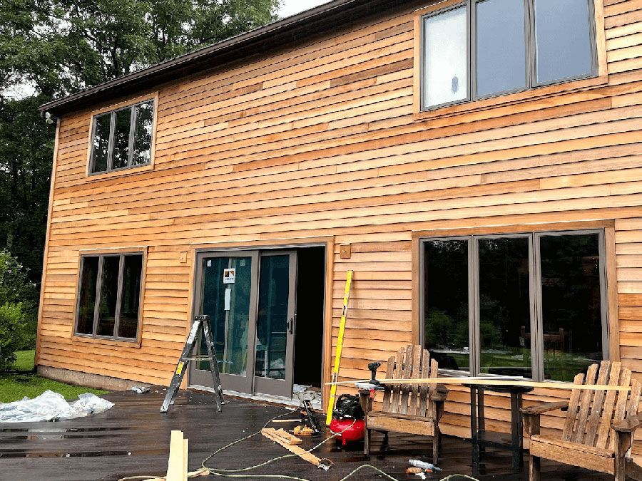 Exterior view of a two-story house with natural wood siding, large windows, and an open patio door during construction.