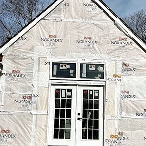 Exterior wall of a building under construction, featuring white house wrap and a set of white French doors with a transom.