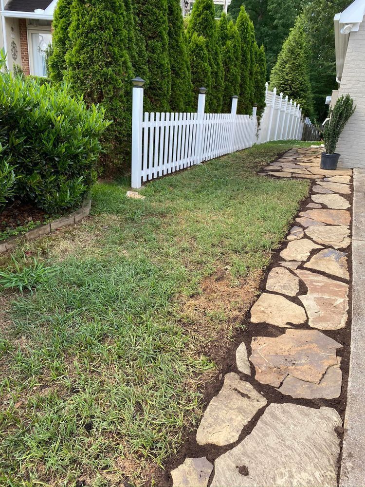 Lawn with stone path, white picket fence, and tall green trees.
