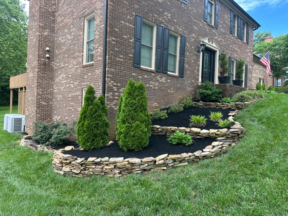 Brick house with tiered stone landscaping, green shrubs, black mulch, and a manicured lawn.