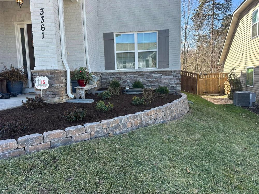 A house with a stacked stone retaining wall and flower bed in front of a lawn.