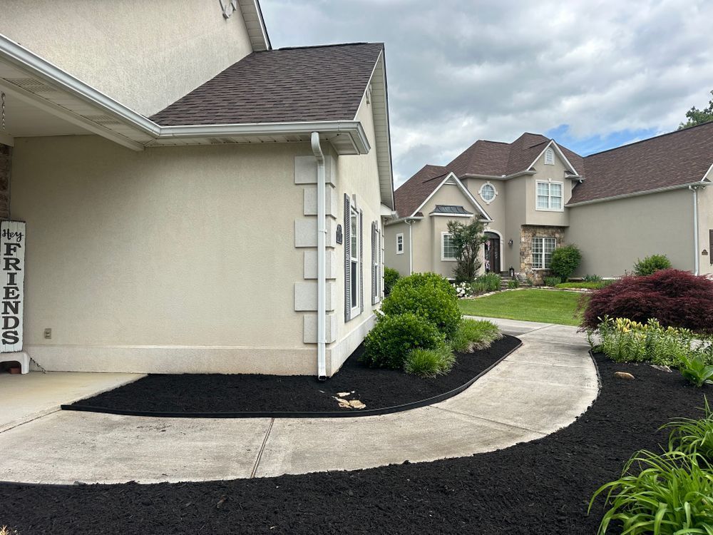 A beige house with dark mulch and a curved sidewalk. Another house is in the background.
