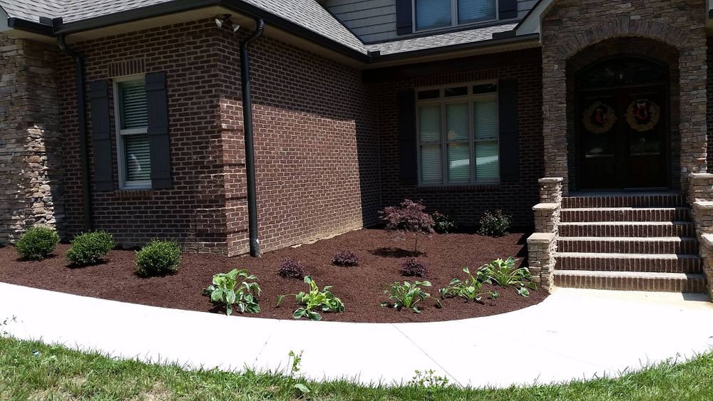 Brown brick house with landscaping, featuring a flower bed with mulch and plants.