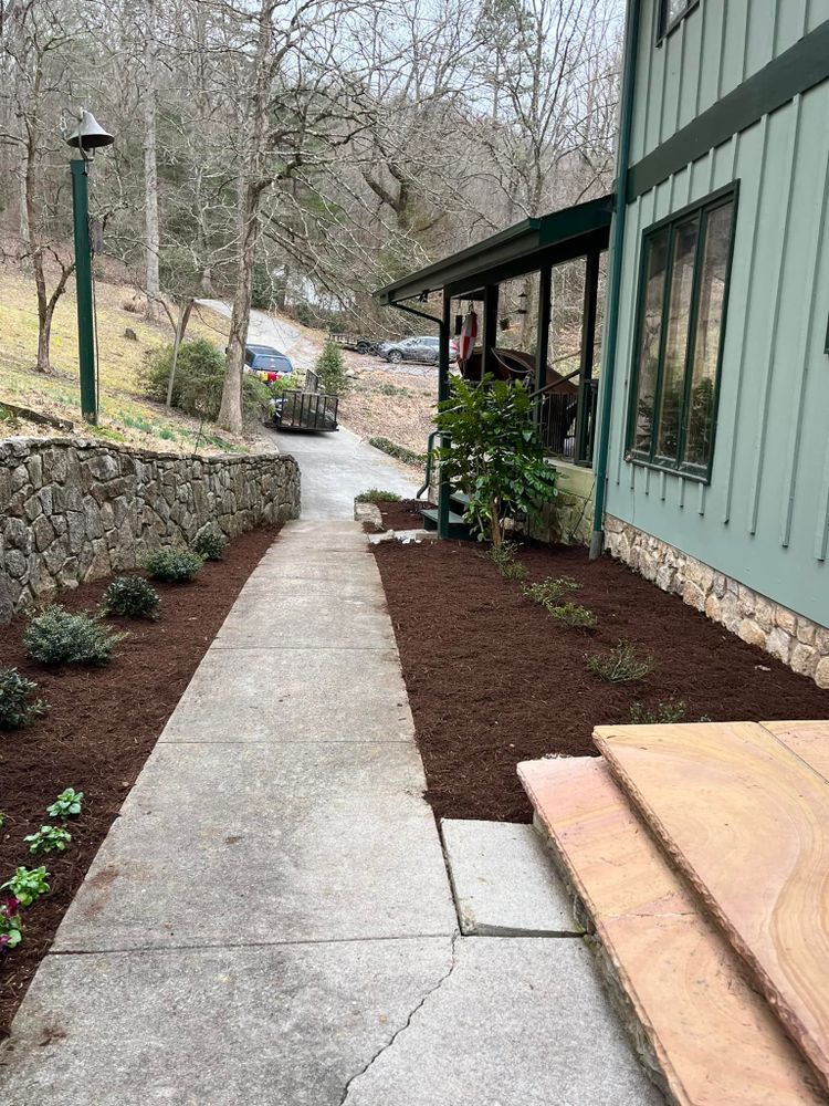 Concrete pathway alongside building and rock wall with fresh mulch and landscaping.