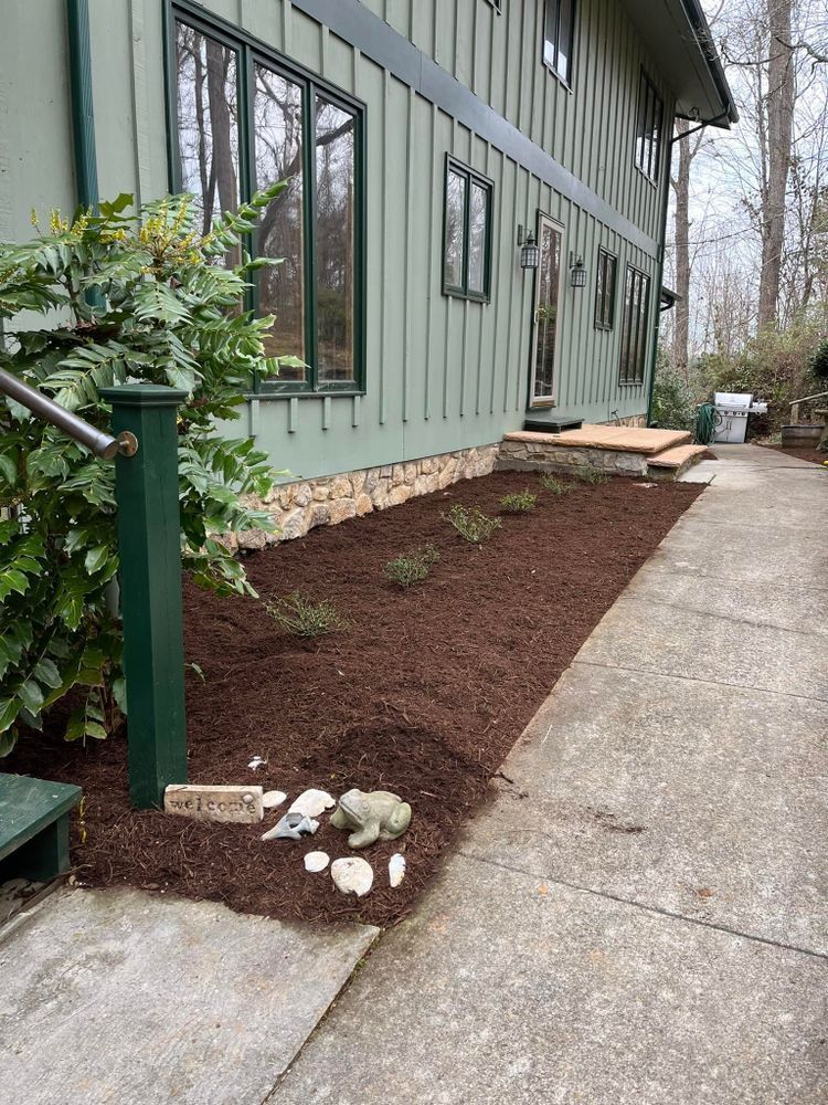 Green house exterior with brown mulch bed, walkway, and small plants.