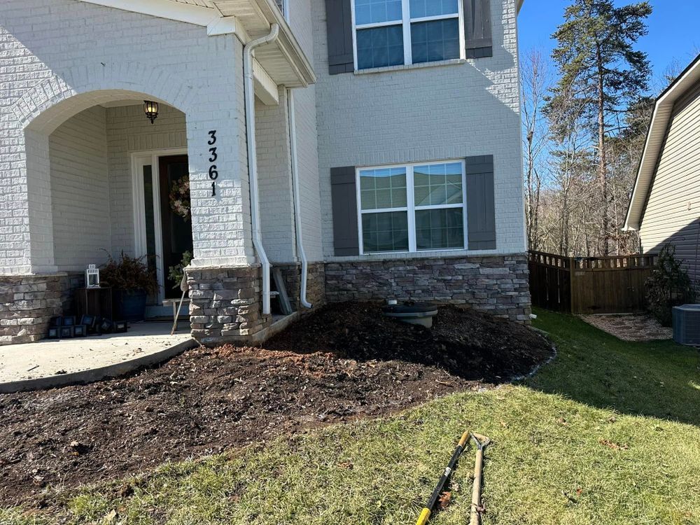 Front of house with mulch in the yard, tools lying on the grass.