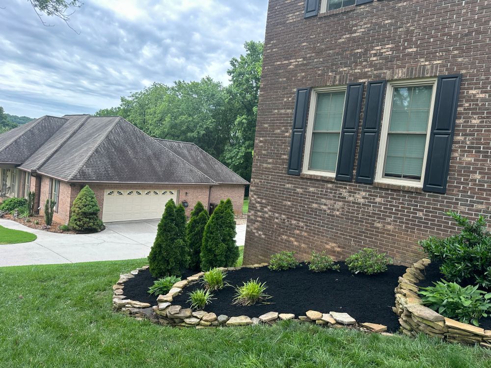 Brick house with black shutters, landscaping, and a garage on a cloudy day.