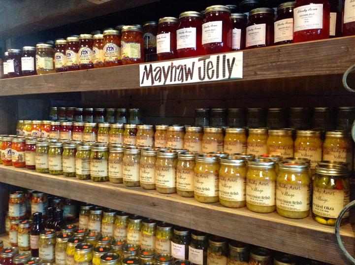 Jarred Mayhaw Jelly with other jarred delicacies underneath it on the shelf