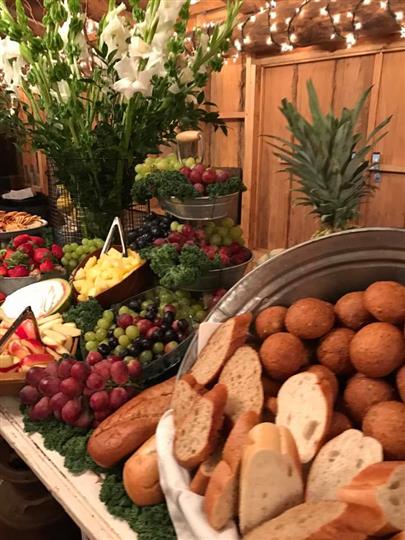 Grapes and bread on a table along with other fruits such as apples, pineapples, and strawberries