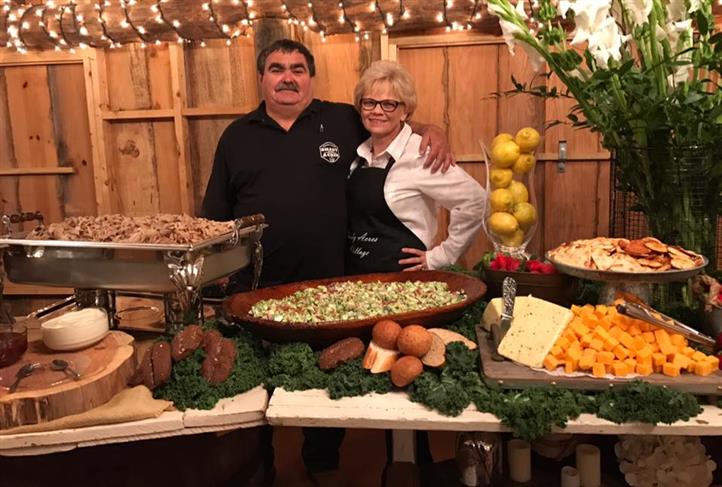 Man and lady smiling taking a photo behind a table filled with foods