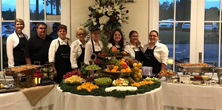 Group photo of caterers standing behind an assortment of fruits on a table