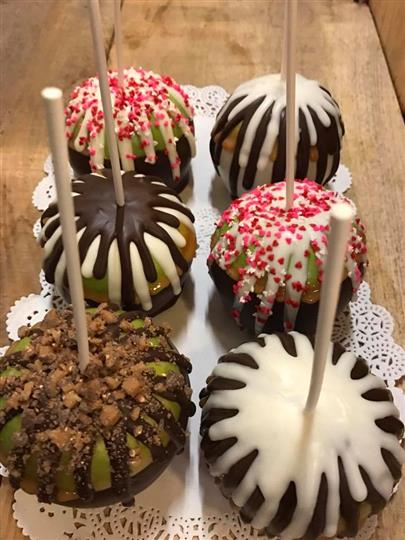 Chocolate dipped apples on a stick with sprinkles and crumbles topped on it