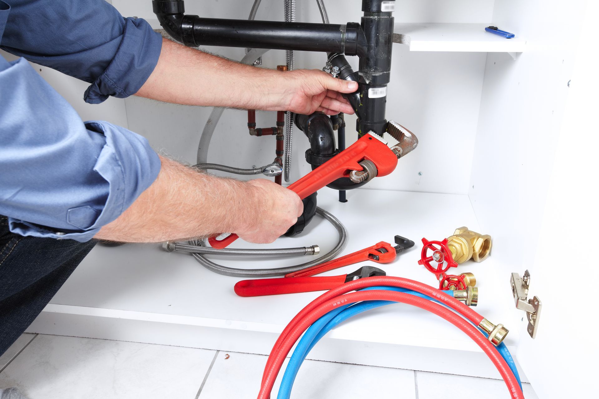 A professional local plumbing contractor with a red pipe wrench to repair a sink drain.